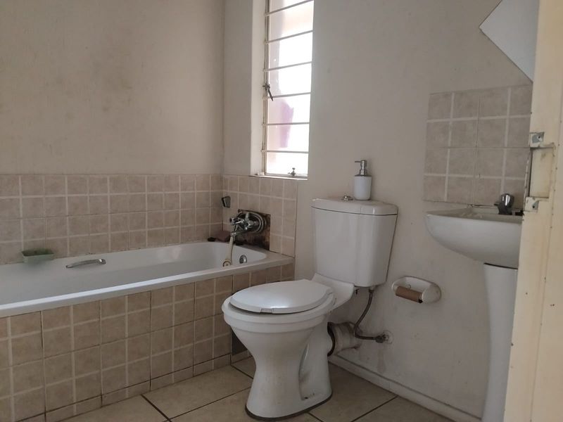 A functional bathroom featuring a bathtub, pedestal basin, and toilet, with tiled splashbacks and security bars on the window.