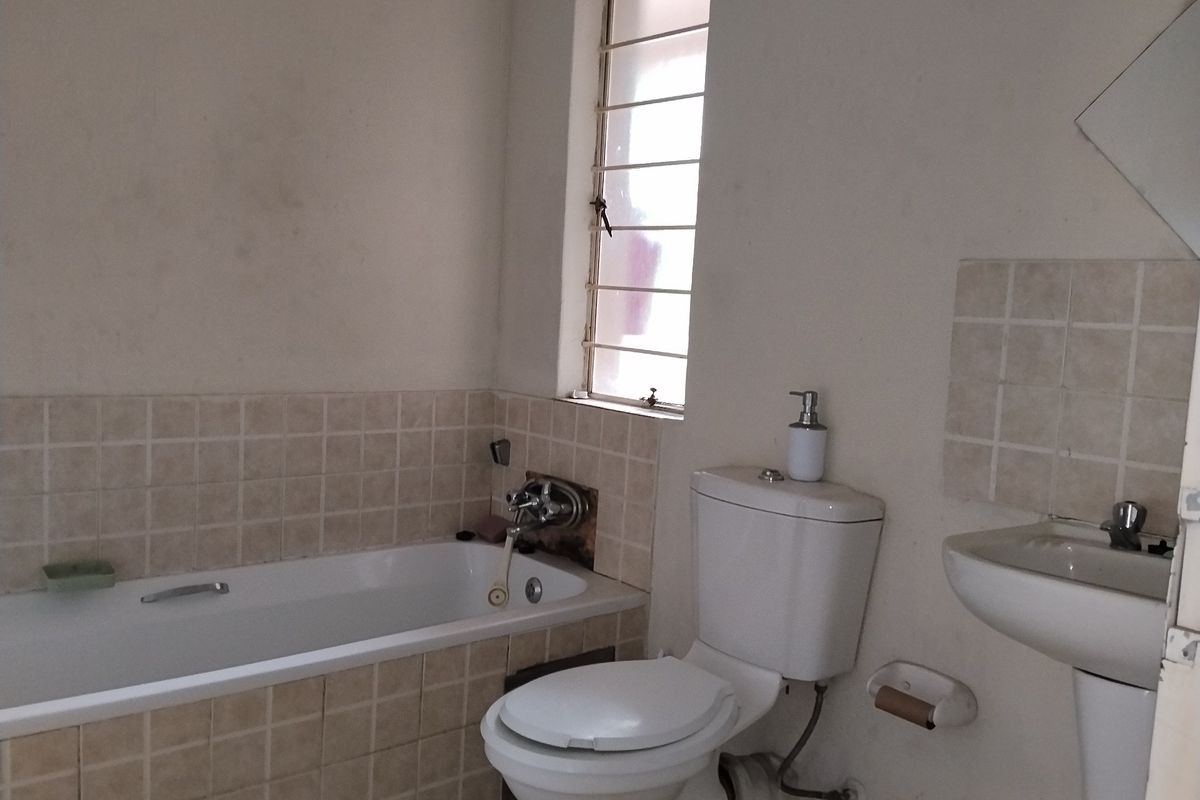 A functional bathroom featuring a bathtub, pedestal basin, and toilet, with tiled splashbacks and a window with security bars.