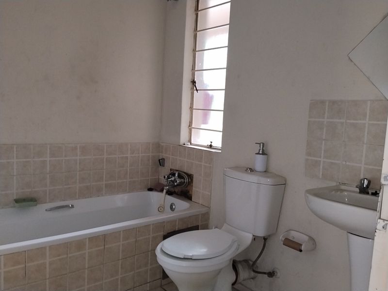 A functional bathroom featuring a bathtub, pedestal basin, and toilet, with tiled splashbacks and a window with security bars.