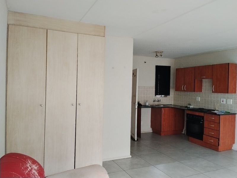Open plan living area featuring a functional kitchen with built-in cabinetry, oven, hob, and tiled flooring, complemented by ample built-in storage cupboards.
