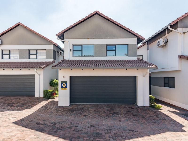 Front elevation of a double-storey townhouse featuring a paved driveway, single garage, and tiled roof with modern aluminium window frames.