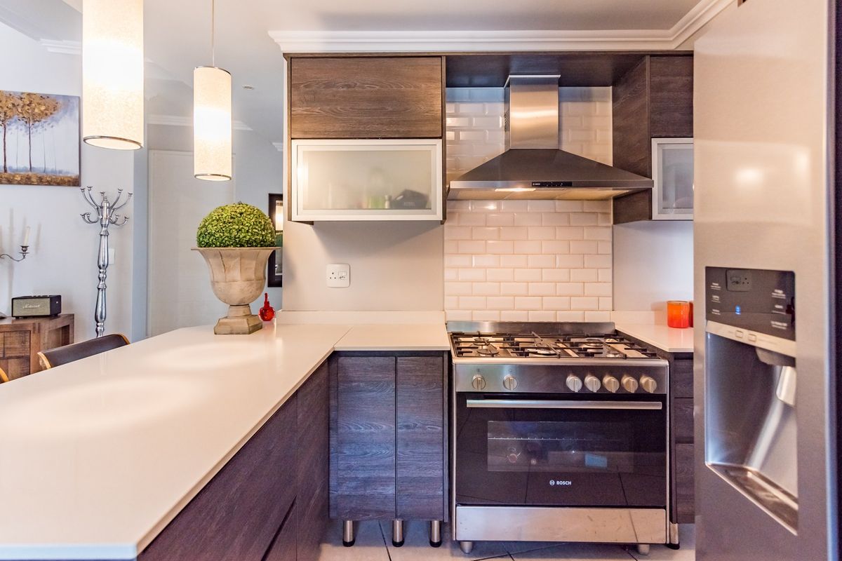 Modern kitchen featuring dark wood cabinetry, quartz countertops, subway tile backsplash, and stainless steel appliances including a gas stove and extractor fan.