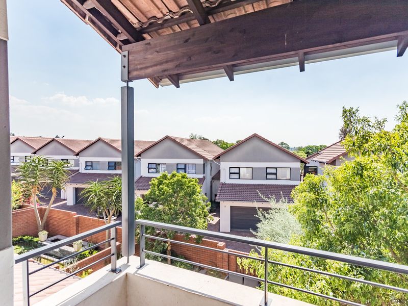 A covered balcony with a metal railing, offering an elevated view over the surrounding townhouse complex and landscaped gardens.