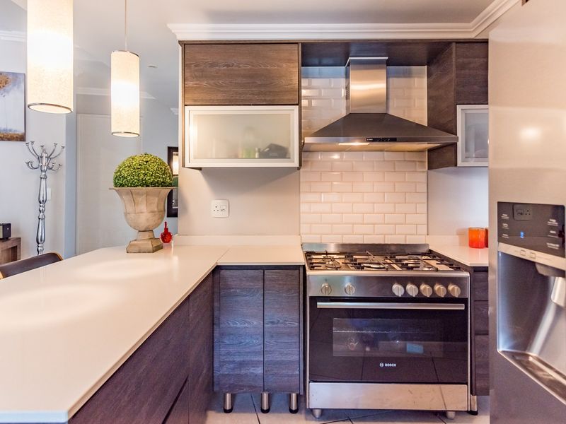 Modern kitchen featuring dark wood cabinetry, quartz countertops, subway tile backsplash, and stainless steel appliances including a gas stove and extractor fan.