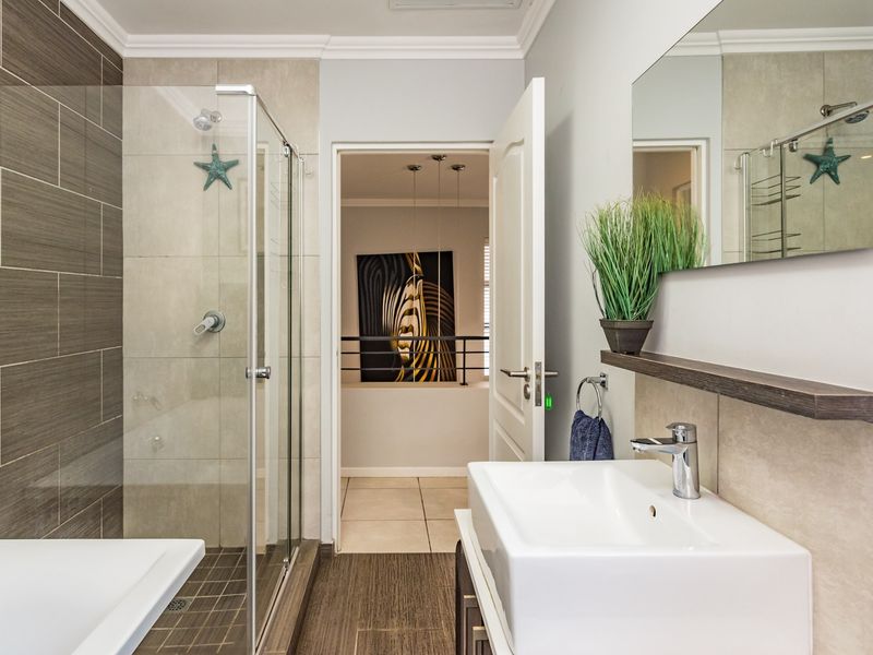 Modern bathroom featuring a glass-enclosed shower, contemporary wall-mounted basin with mixer tap, and neutral tiled finishes.
