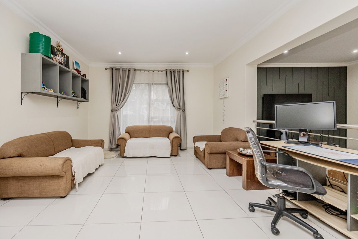 Spacious living area featuring large format floor tiles, recessed lighting, and a modern feature wall, offering a versatile layout for relaxation and home office use.