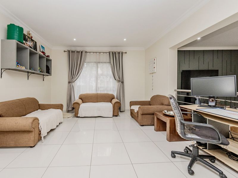 Spacious living area featuring large format floor tiles, recessed lighting, and a modern feature wall, offering a versatile layout for relaxation and home office use.