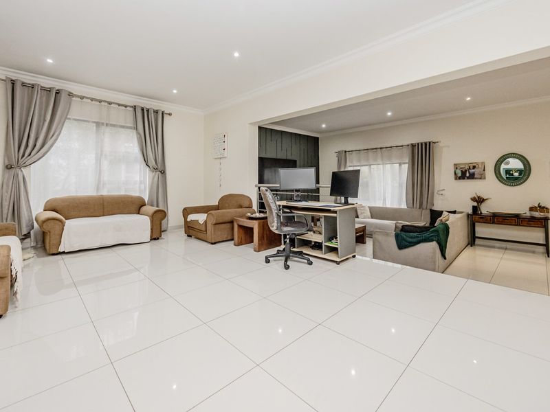 Spacious open-plan living area featuring polished porcelain floor tiles, recessed downlighting, and a modern feature wall, offering a versatile layout for various living arrangements.
