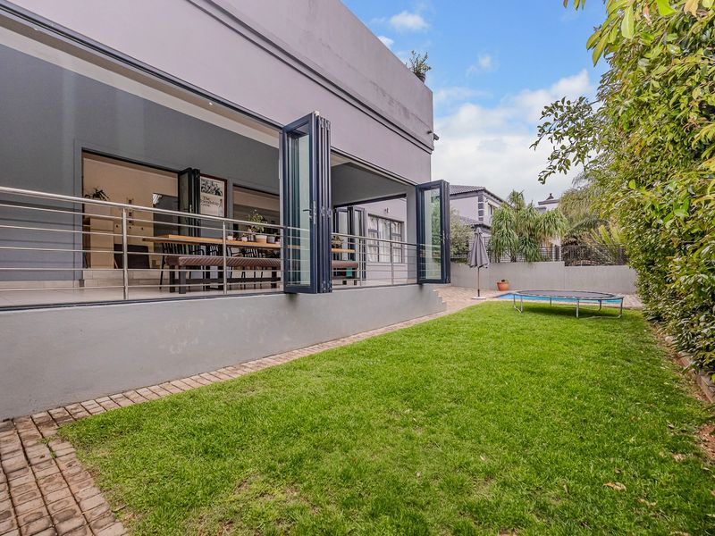 Rear view of the property featuring a landscaped garden, swimming pool, and a covered patio area accessible through large bi-fold doors.