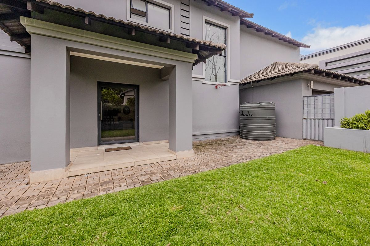 A well-maintained rear exterior view featuring a paved patio area, a water storage tank, and a neat lawn adjacent to the house structure.