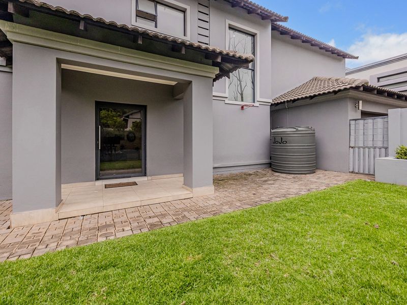 A well-maintained rear exterior view featuring a paved patio area, a water storage tank, and a neat lawn adjacent to the house structure.