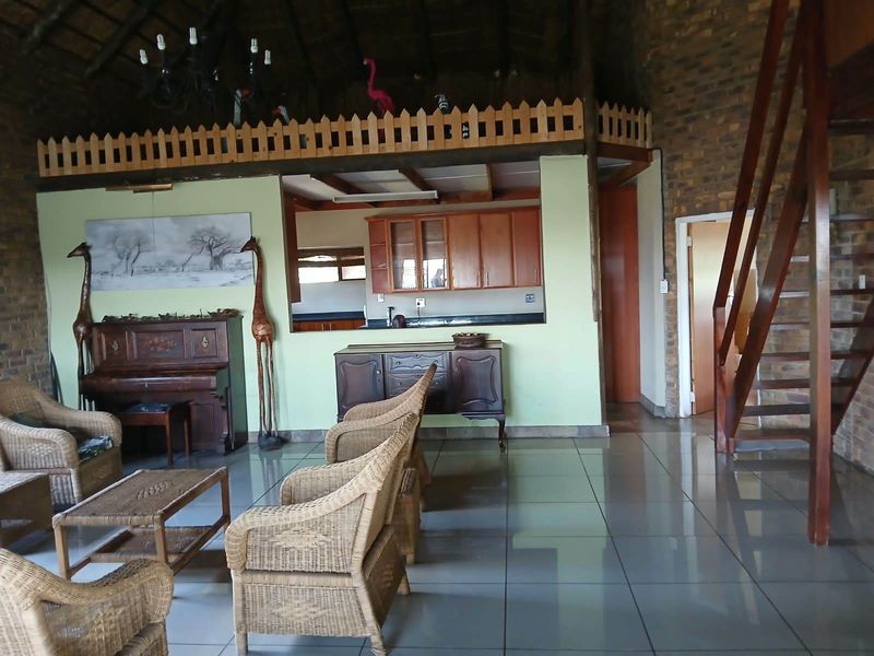 Open plan living area featuring a thatched roof, exposed brick walls, tiled floors, and a mezzanine level overlooking the kitchen and living space.