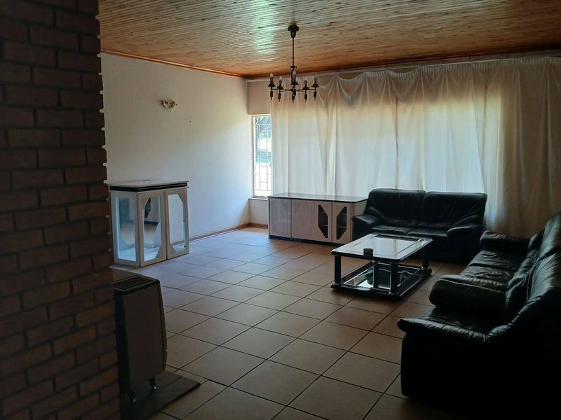 Spacious living room featuring tiled flooring, a timber ceiling, and an exposed brick accent wall, offering a functional and traditional layout.
