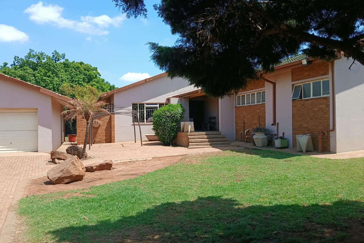 Rear view of the farm property featuring a paved patio area, attached garage, and established garden space with brick and rendered wall finishes.