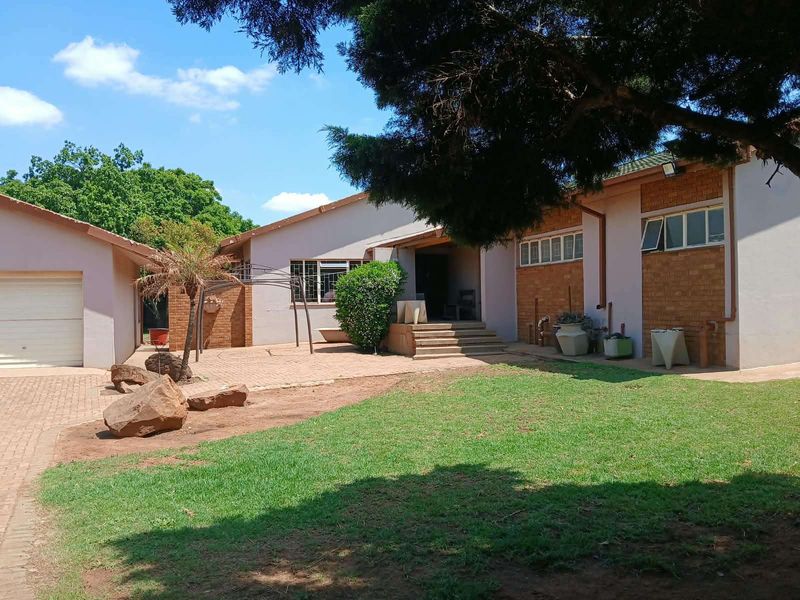 Rear view of the farm property featuring a paved patio area, attached garage, and established garden space with brick and rendered wall finishes.