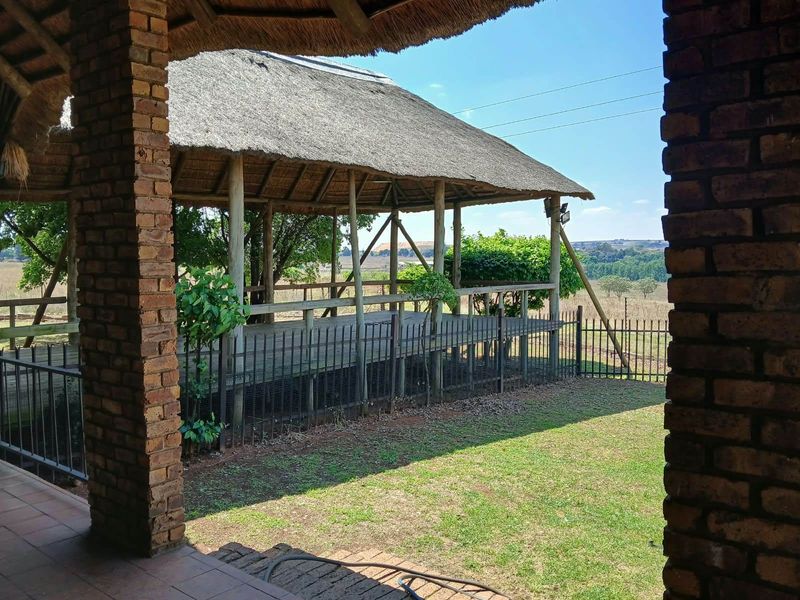A spacious outdoor entertainment area featuring a thatched roof, timber decking, and brick pillars, overlooking the surrounding farm landscape.