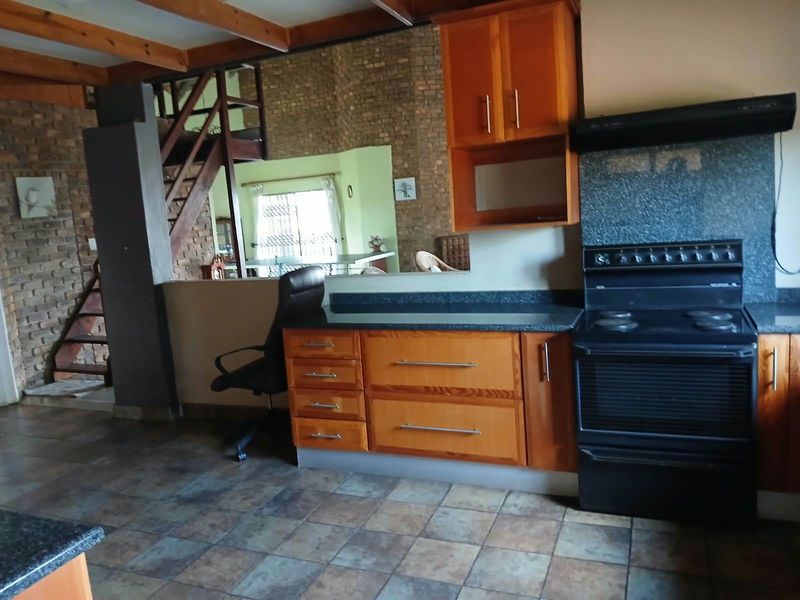 Kitchen featuring wooden cabinetry, stone countertops, and a freestanding stove, set against a rustic brick wall with exposed timber ceiling beams.