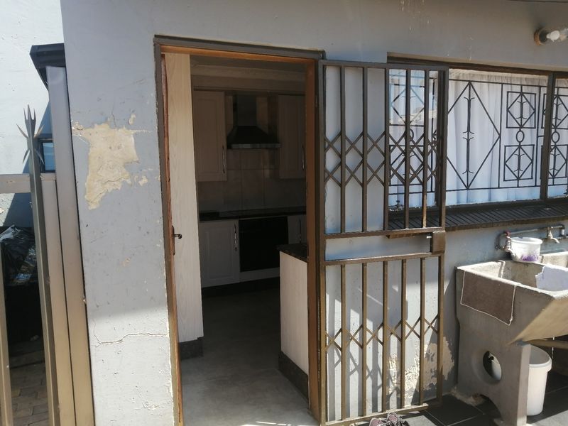 Exterior view of a utility area featuring a concrete laundry sink, security gate, and access to a kitchen with built-in cabinetry and appliances.