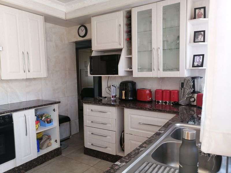 Functional kitchen featuring white cabinetry, granite countertops, a double bowl sink, and built-in appliances, offering a practical layout with ample storage space.