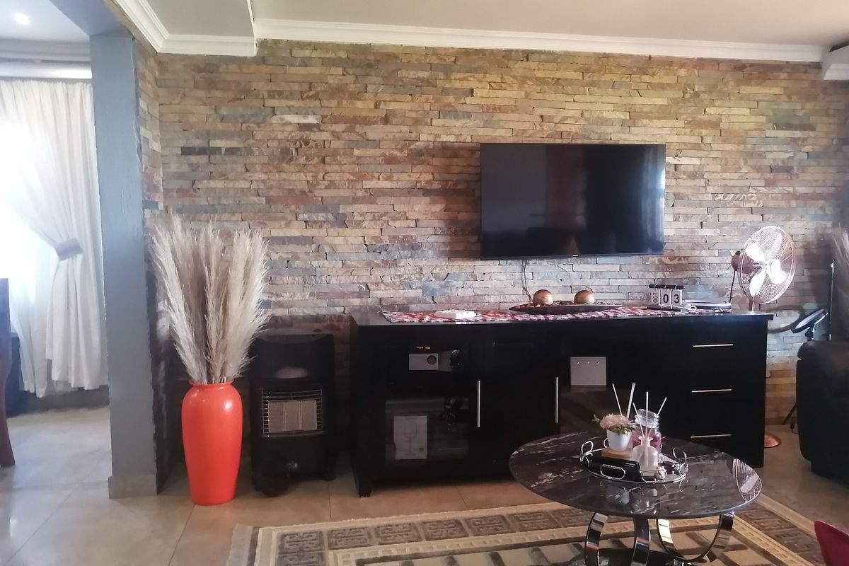 A living room featuring a prominent stacked stone accent wall, tiled flooring, and recessed ceiling lighting.