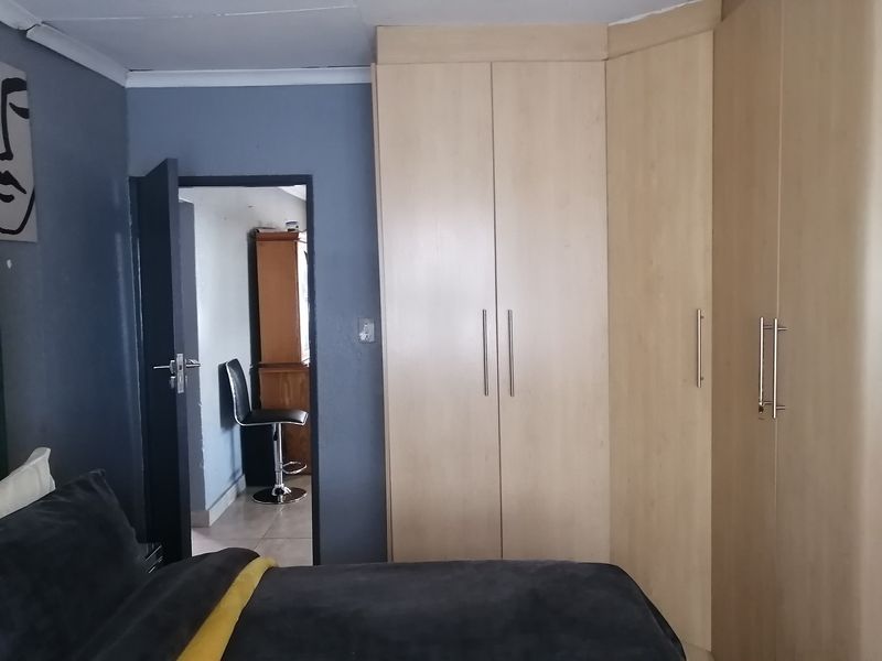 A bedroom featuring light wood-toned built-in cupboards and blue-painted walls, with a doorway leading to an adjacent space.