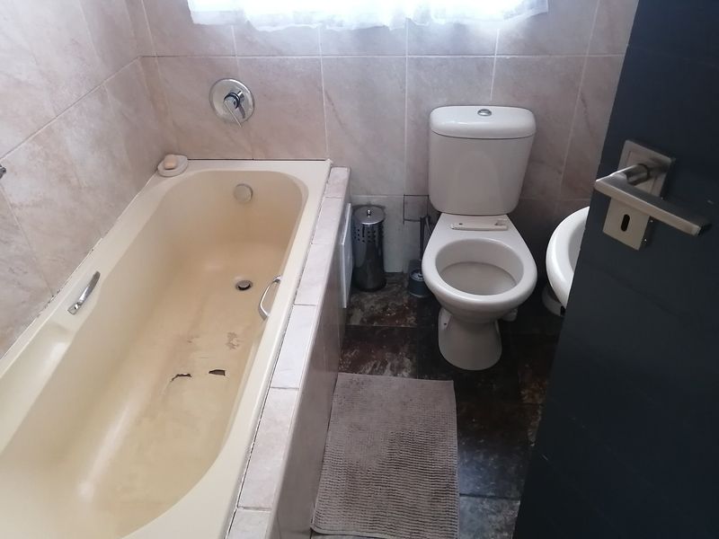 A compact bathroom featuring a built-in bathtub, toilet, and washbasin with tiled finishes. The bathtub shows signs of wear and surface damage.