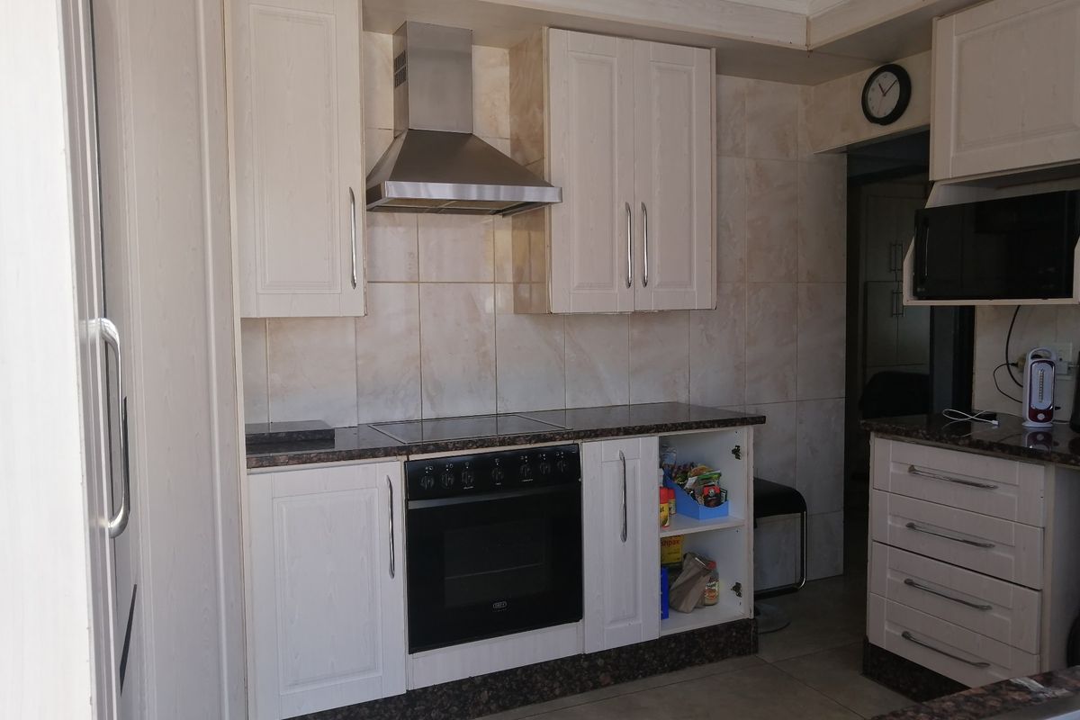 A functional kitchen featuring built-in cabinetry, granite countertops, a stainless steel extractor fan, and a built-in oven with a ceramic hob.