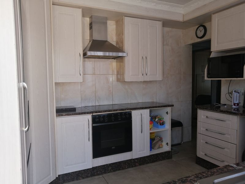 A functional kitchen featuring built-in cabinetry, granite countertops, a stainless steel extractor fan, and a built-in oven with a ceramic hob.