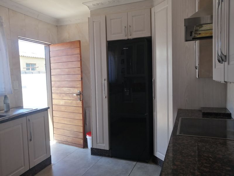 A functional kitchen featuring white cabinetry, granite countertops, an integrated hob, and an extractor fan, with direct access to the exterior.