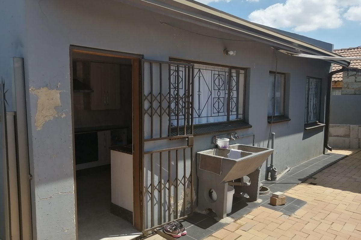 Rear exterior view of the property featuring a paved patio area, a concrete laundry sink, and security gates on the entrance.
