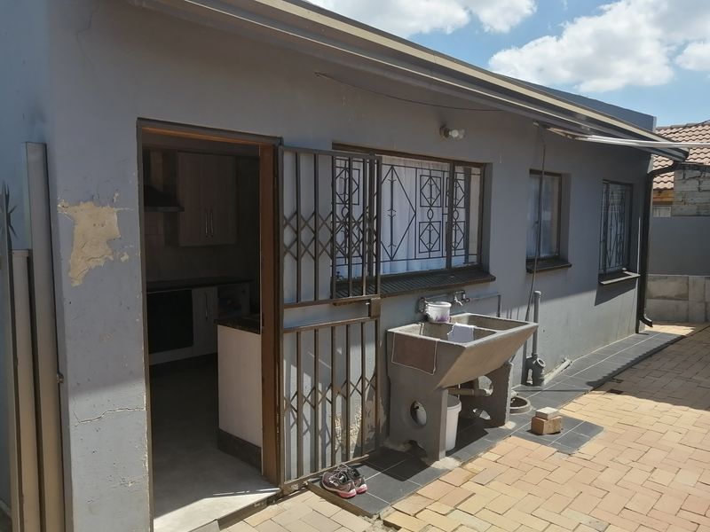 Rear exterior view of the property featuring a paved patio area, a concrete laundry sink, and security gates on the entrance.