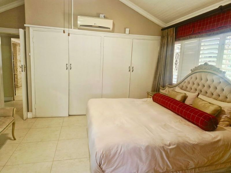 A spacious bedroom featuring vaulted ceilings, tiled flooring, built-in cupboards, and a wall-mounted air conditioning unit.