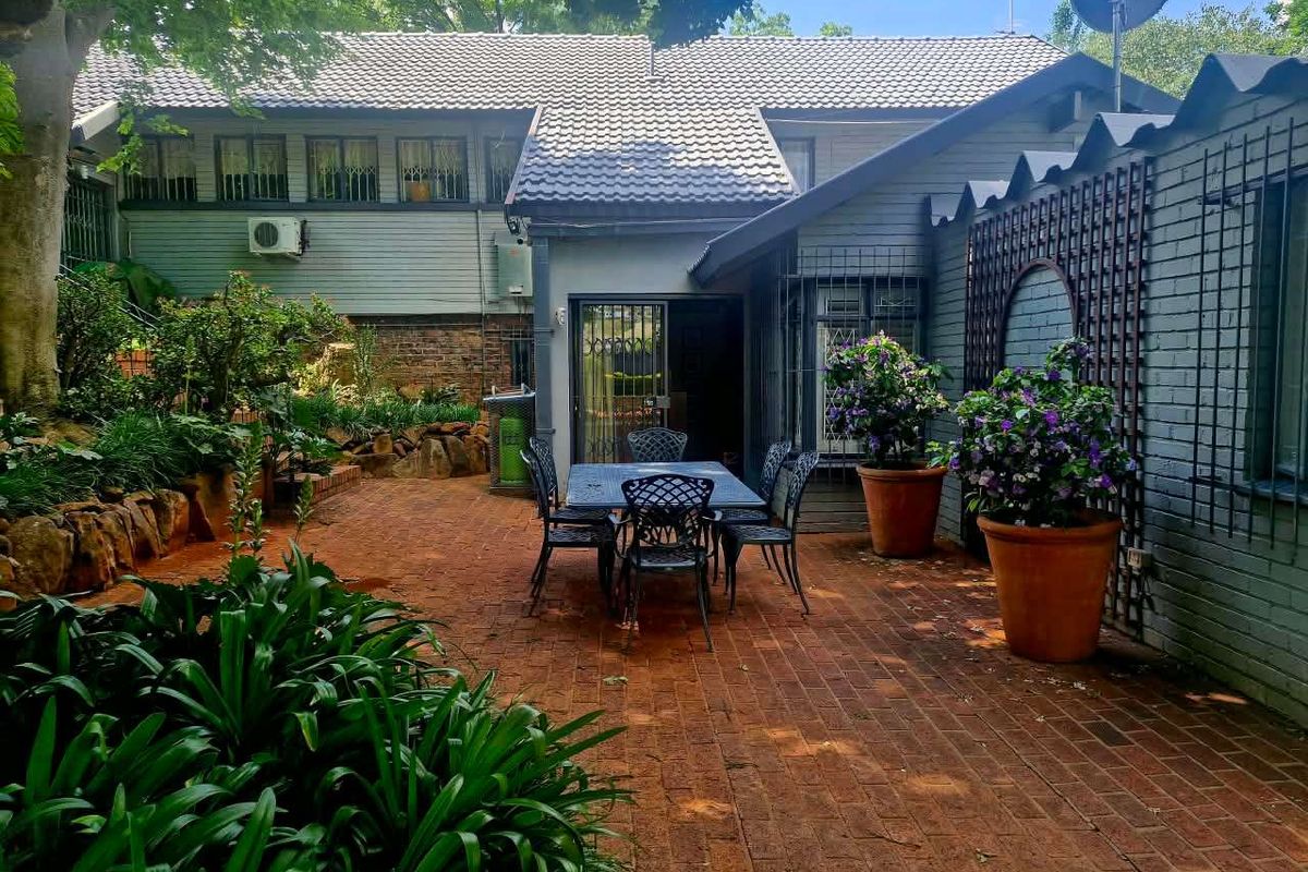 A private rear patio area featuring brick paving, established garden surroundings, and direct access to the home through a sliding glass door.