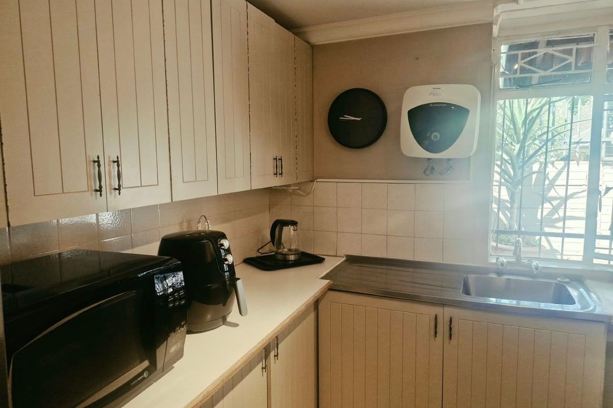Compact kitchen featuring built-in cabinetry, a stainless steel sink, tiled backsplash, and an integrated electric water heater.