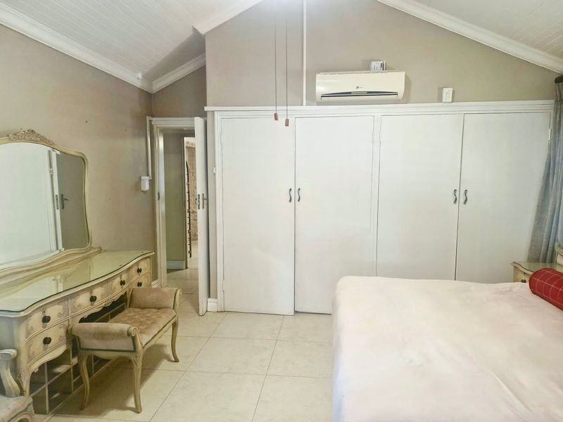 Spacious bedroom featuring vaulted ceilings, tiled flooring, extensive built-in cupboard storage, and a wall-mounted air conditioning unit.
