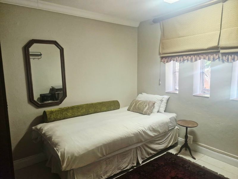 A compact bedroom featuring neutral wall tones, coving, skirting boards, and dual windows fitted with roman blinds.