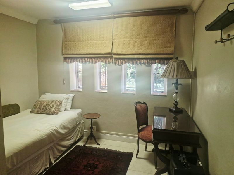 A compact bedroom featuring tiled flooring, neutral wall finishes, and multiple small windows with integrated blinds.