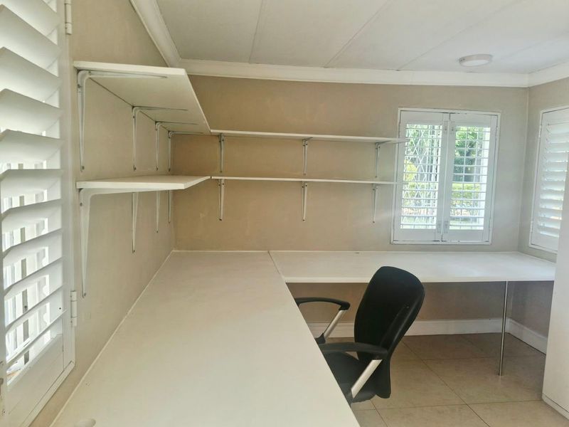 Dedicated home office space featuring built-in desk surfaces, wall-mounted shelving, and plantation shutters for adjustable natural light.
