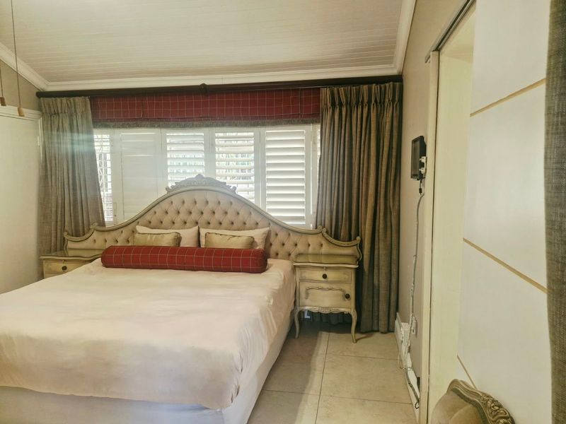 A bedroom featuring tiled flooring, a timber-look ceiling, and plantation shutters. The space includes a sliding door and requires minor electrical cable management.