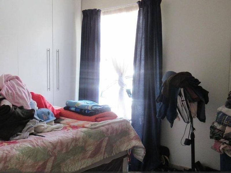 A bedroom featuring built-in cupboards and a window with curtains, providing functional storage and natural light.