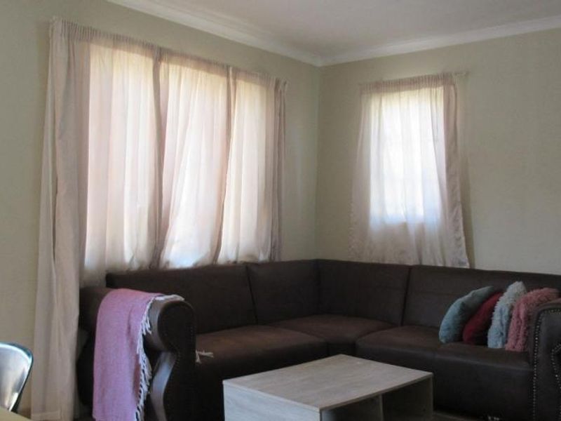 A living room area featuring neutral wall tones, cornice detailing, and natural light through window treatments.
