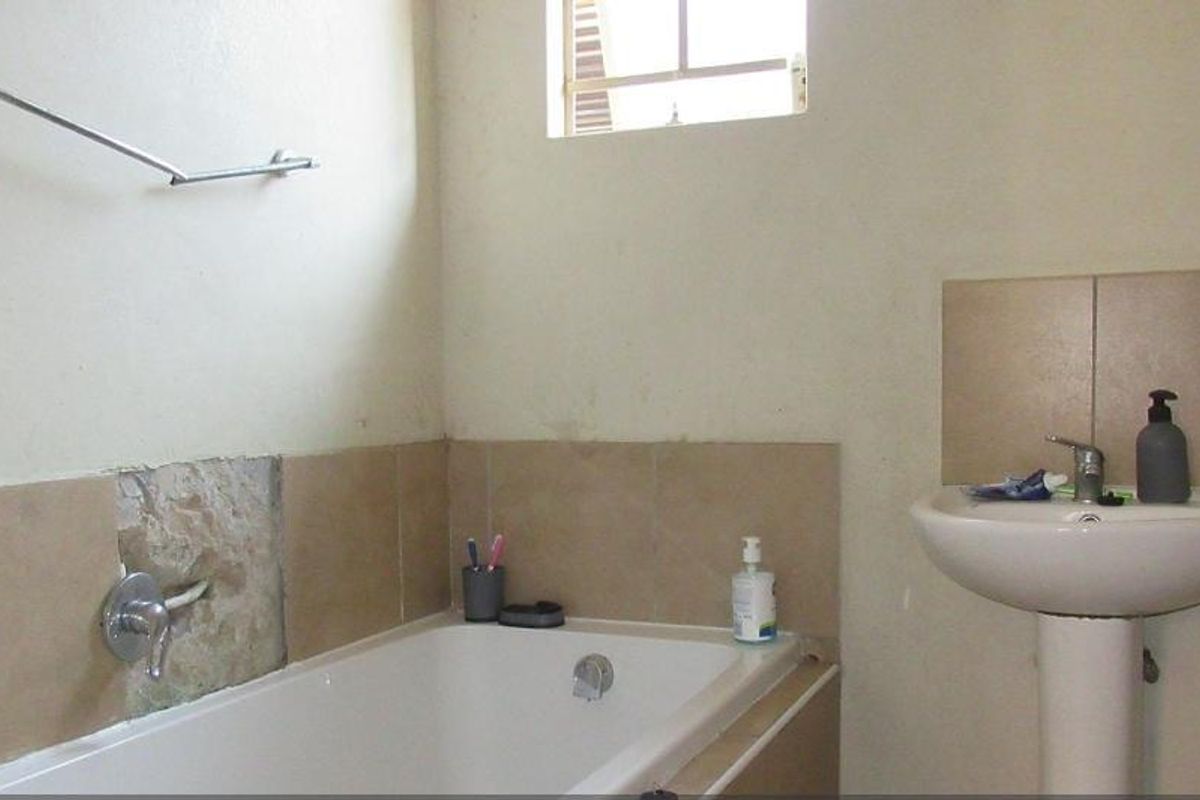 A functional bathroom featuring a pedestal basin and a built-in bathtub with tiled splashbacks, currently requiring minor repairs to wall finishes.