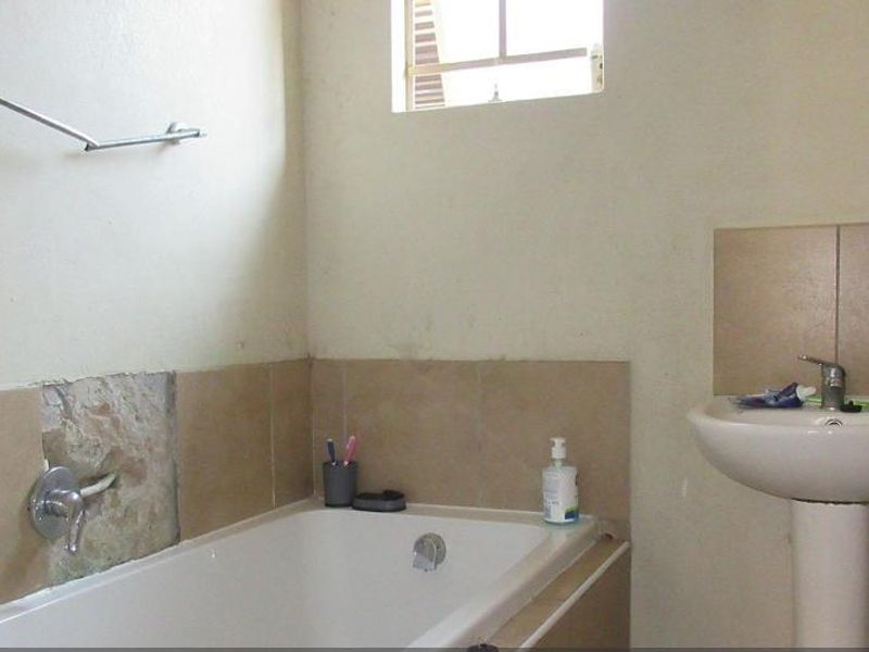 A functional bathroom featuring a pedestal basin and a built-in bathtub with tiled splashbacks, currently requiring minor repairs to wall finishes.