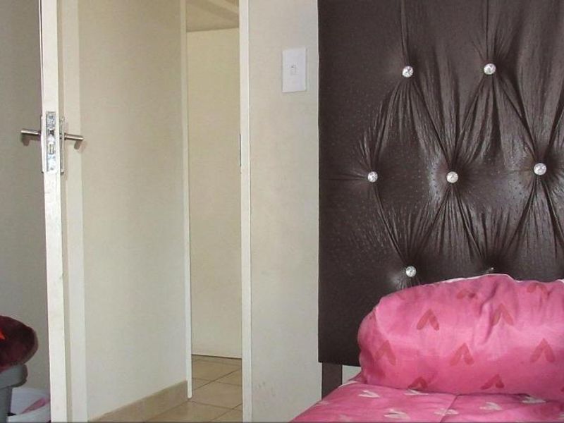 A bedroom interior featuring tiled flooring and a doorway leading to an adjacent space.