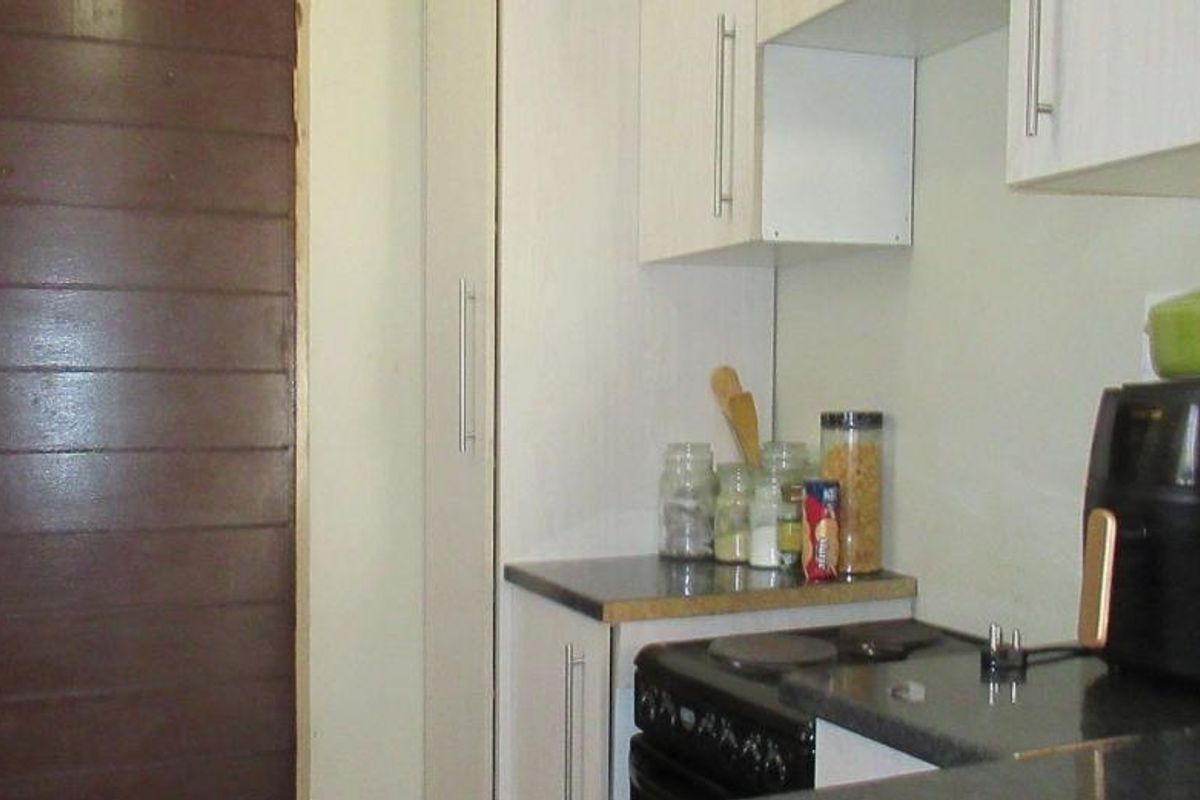 A compact kitchen featuring white built-in cabinetry, dark laminate countertops, and an electric stove, providing a functional workspace.