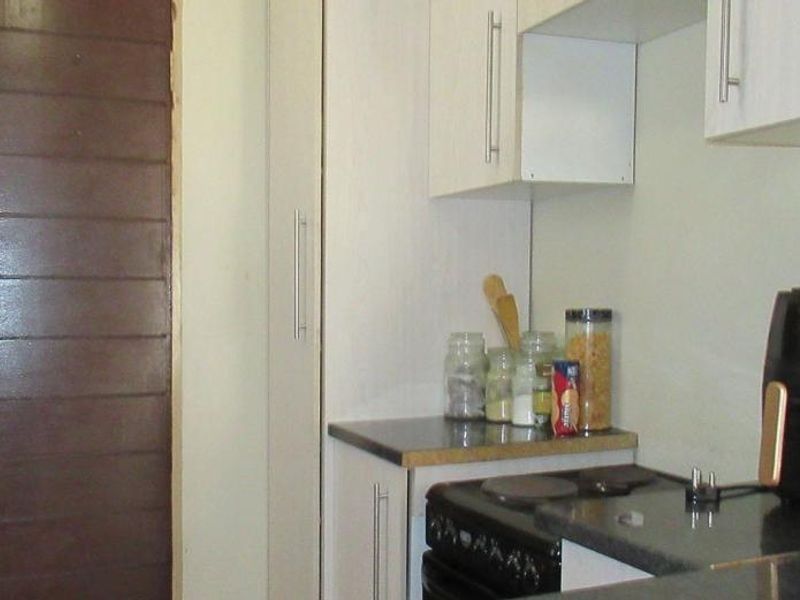 A compact kitchen featuring white built-in cabinetry, dark laminate countertops, and an electric stove, providing a functional workspace.