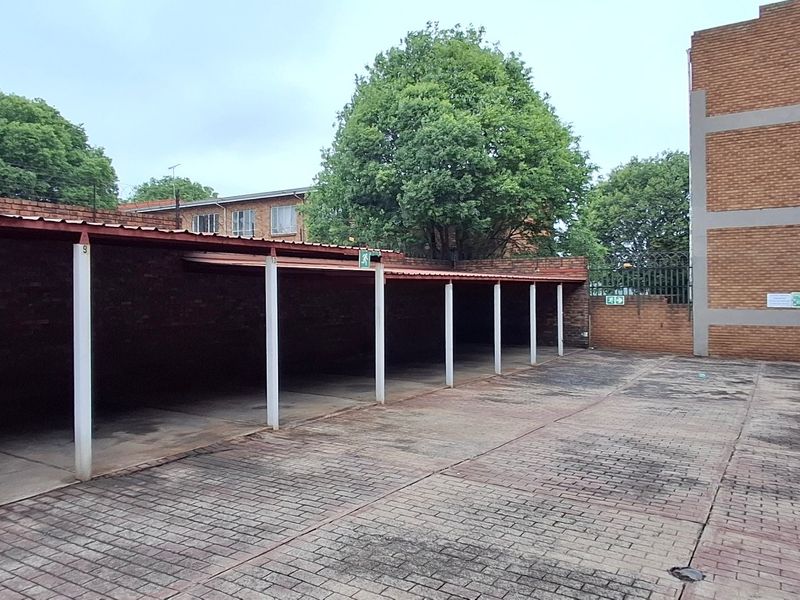 An open-air parking area featuring multiple covered parking bays with brick paving and secure perimeter fencing within the apartment complex.