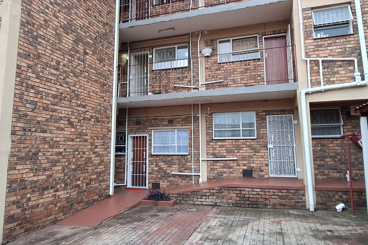 Rear view of a multi-story apartment building featuring face brick construction, security gates, and a paved courtyard area.