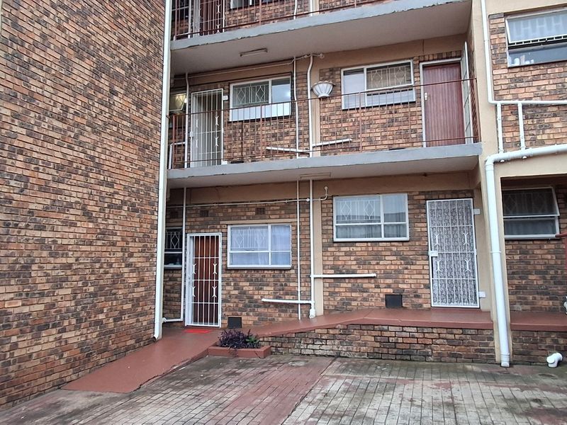 Rear view of a multi-story apartment building featuring face brick construction, security gates, and a paved courtyard area.