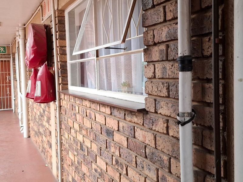 An exterior apartment corridor featuring exposed brick walls, metal security gates, and fire safety equipment along the walkway.